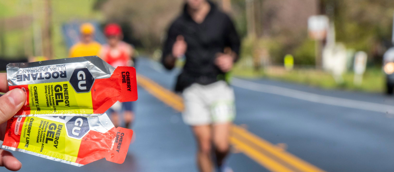 2 GU Cherry Lime Roctane Energy Gels with people running a road race in the background