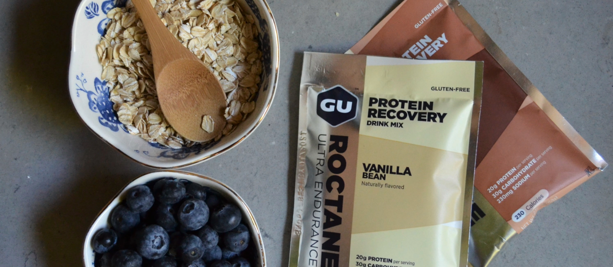 GU Vanilla Bean Roctane Protein Recovery Drink Mix with blueberries and oats on a table