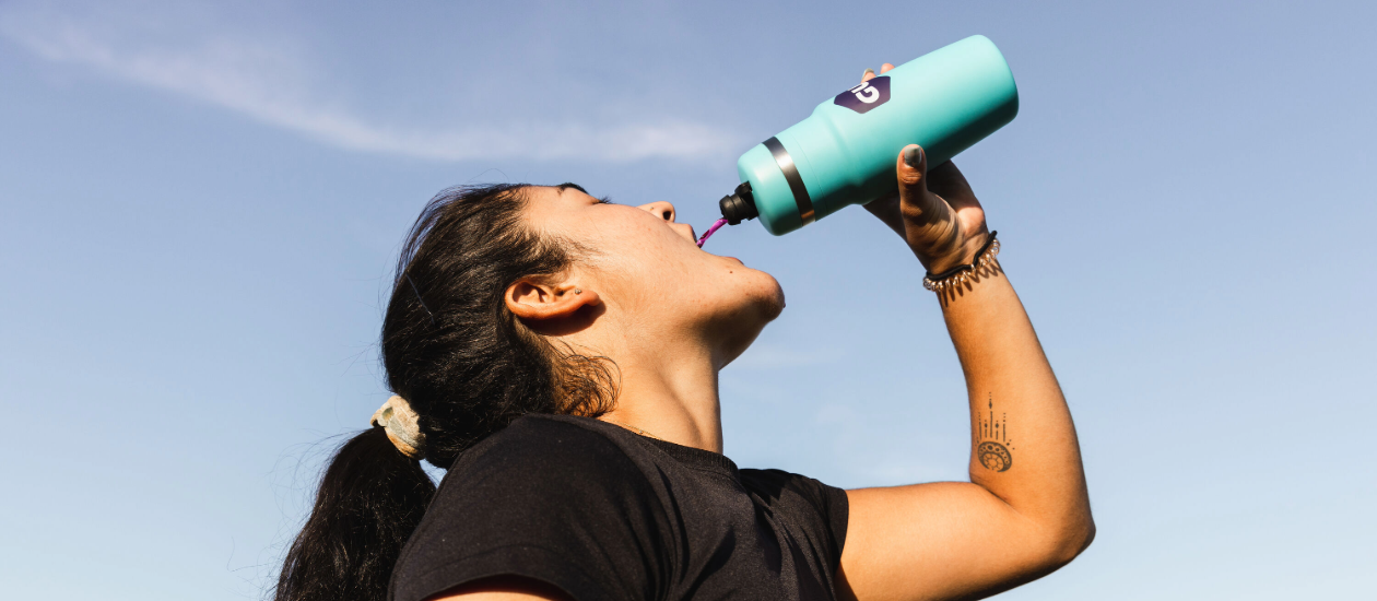 woman drinking out of a GU bivo bottle with blue sky in the background